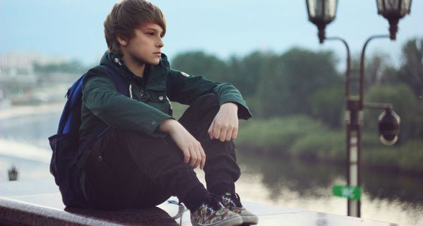Ein Junge, etwa 11 bis 14 Jahre alt, sitzt alleine und schaut nachdenklich.