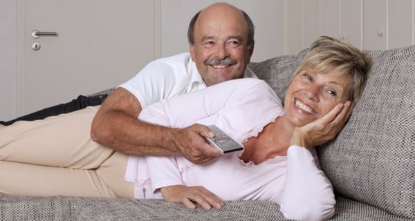 Frau und Mann liegen auf dem Sofa und sehen fern.