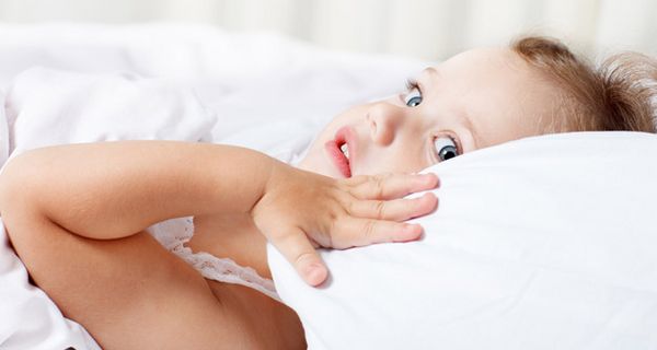 Kleines Mädchen liegt wach im Bett und schaut betrübt.