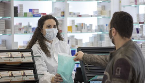 Apothekerin mit Maske übergibt eine Tüte an Patienten.
