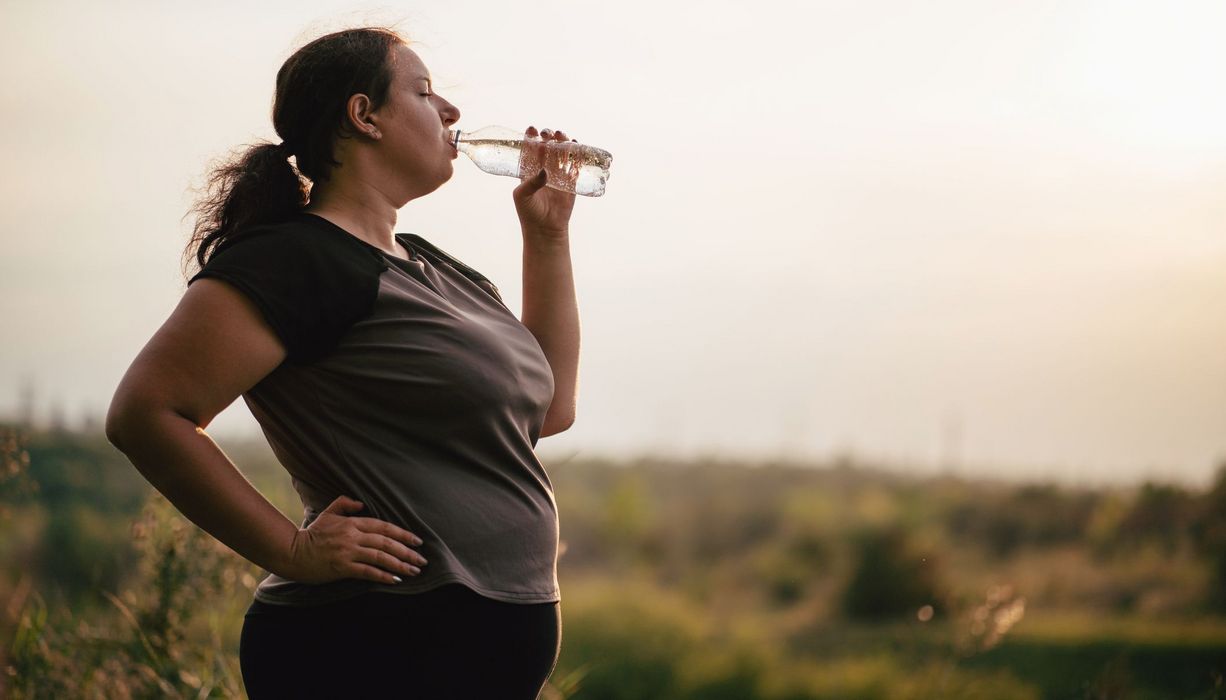 Übergewichtige Frau, trinkt Wasser.