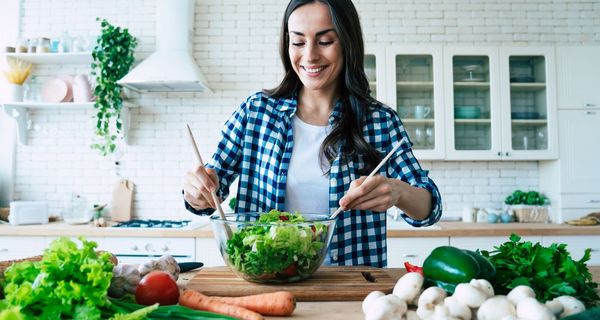 Frau mischt sich einen grünen Salat in einer Küche.