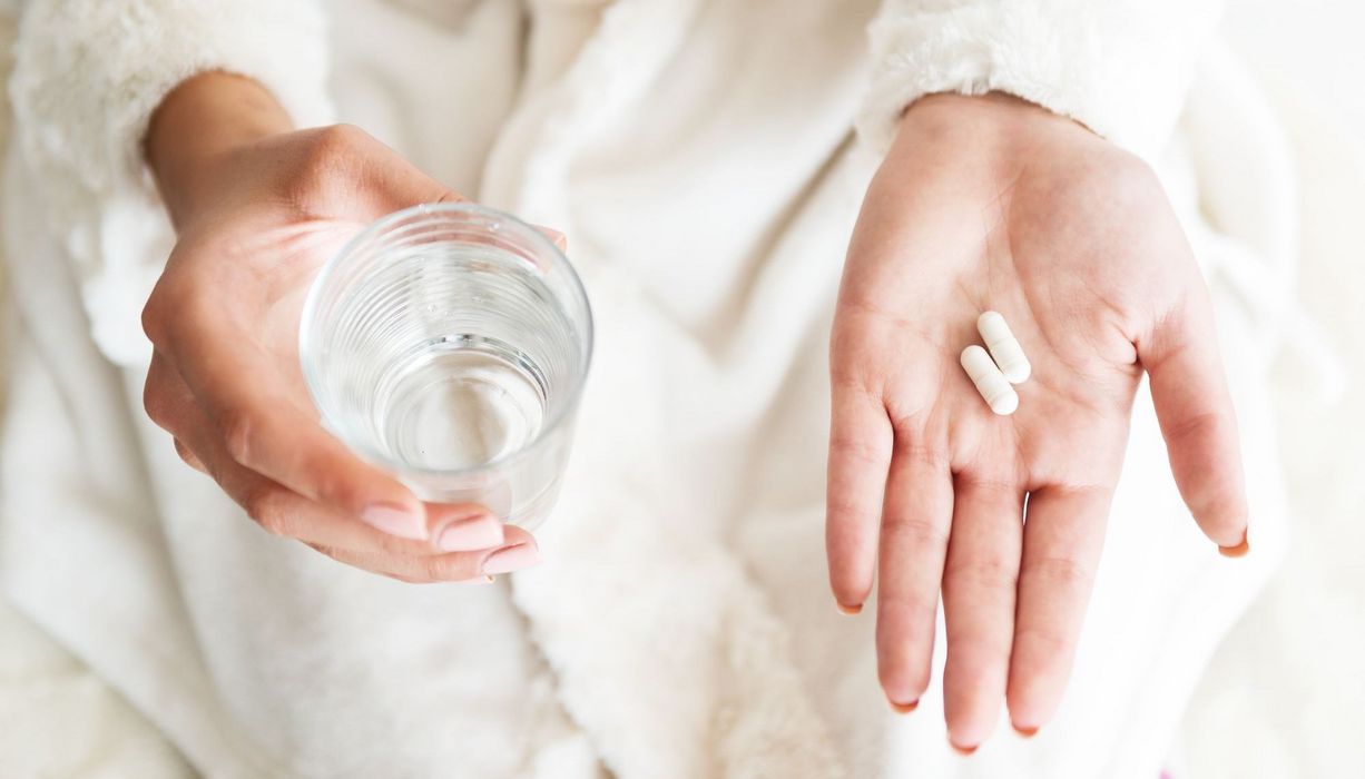 Frau, hält in einer Hand Tabletten und in der anderen Hand ein Glas Wasser.