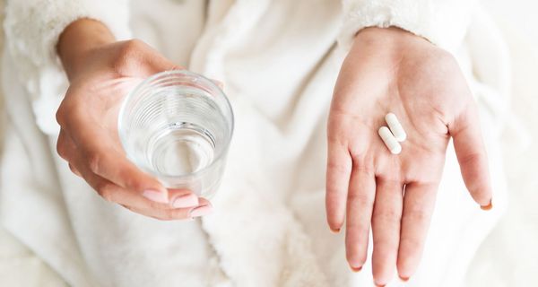 Frau, hält in einer Hand Tabletten und in der anderen Hand ein Glas Wasser.