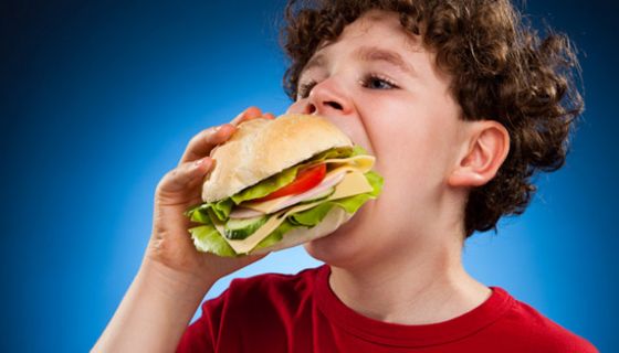 Junge mit Locken beißt in einen riesig großen Burger