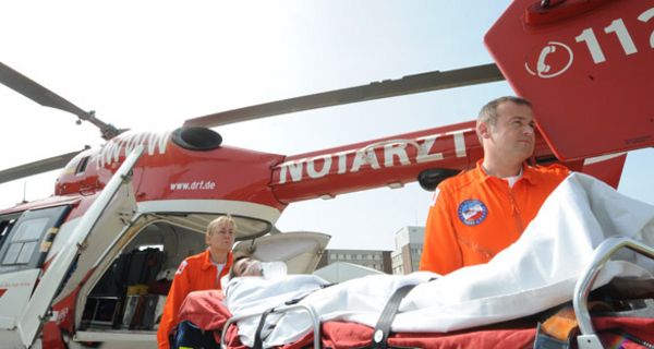 Notarzteinsatz mit Hubschrauber, davor Notärte und Patientin auf Trage mit Sauerstoffmaske