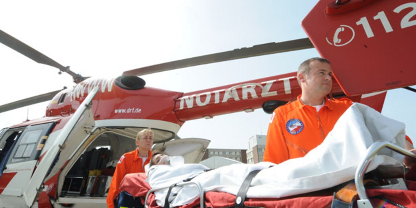 Notarzteinsatz mit Hubschrauber, davor Notärte und Patientin auf Trage mit Sauerstoffmaske