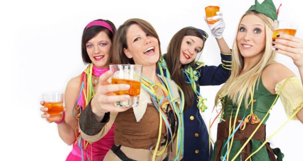 4 lustige Frauen, ca. Mitte 20, in Faschingskostümen mit Drinks prosten in die Kamera