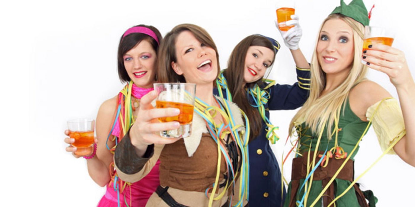4 lustige Frauen, ca. Mitte 20, in Faschingskostümen mit Drinks prosten in die Kamera