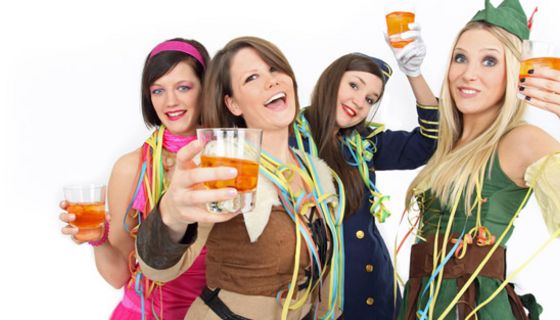 4 lustige Frauen, ca. Mitte 20, in Faschingskostümen mit Drinks prosten in die Kamera