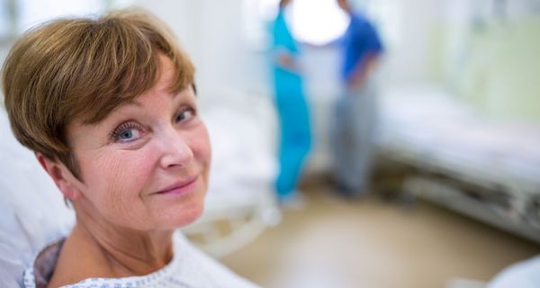 Frau, etwa 50 Jahre alt, sitzt im Krankenhausbett und lächelt.
