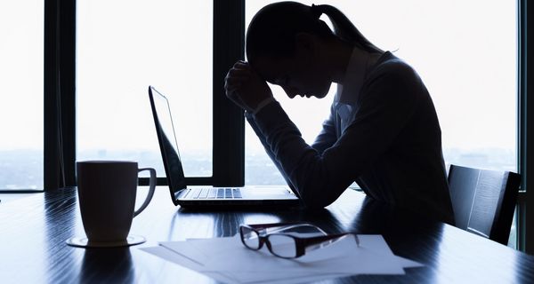 Junge Frau, stützt ihren Kopf auf die Hände und sitzt vor dem Laptop.