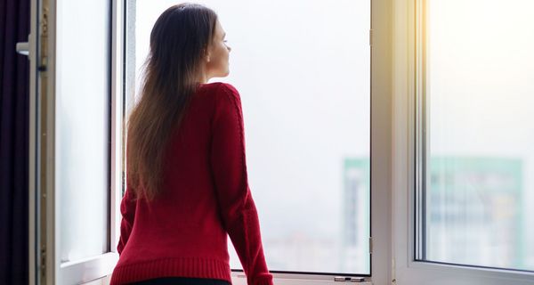 Frau, steht an einem großen offenen Fenster.