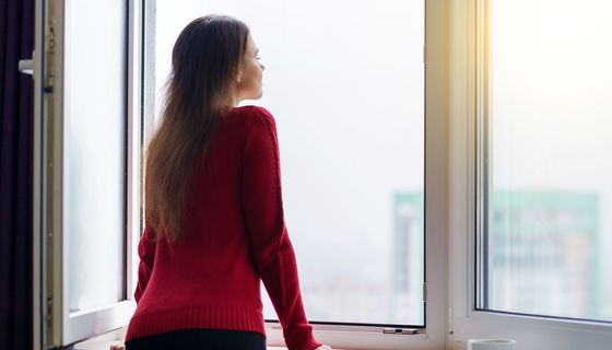 Frau, steht an einem großen offenen Fenster.