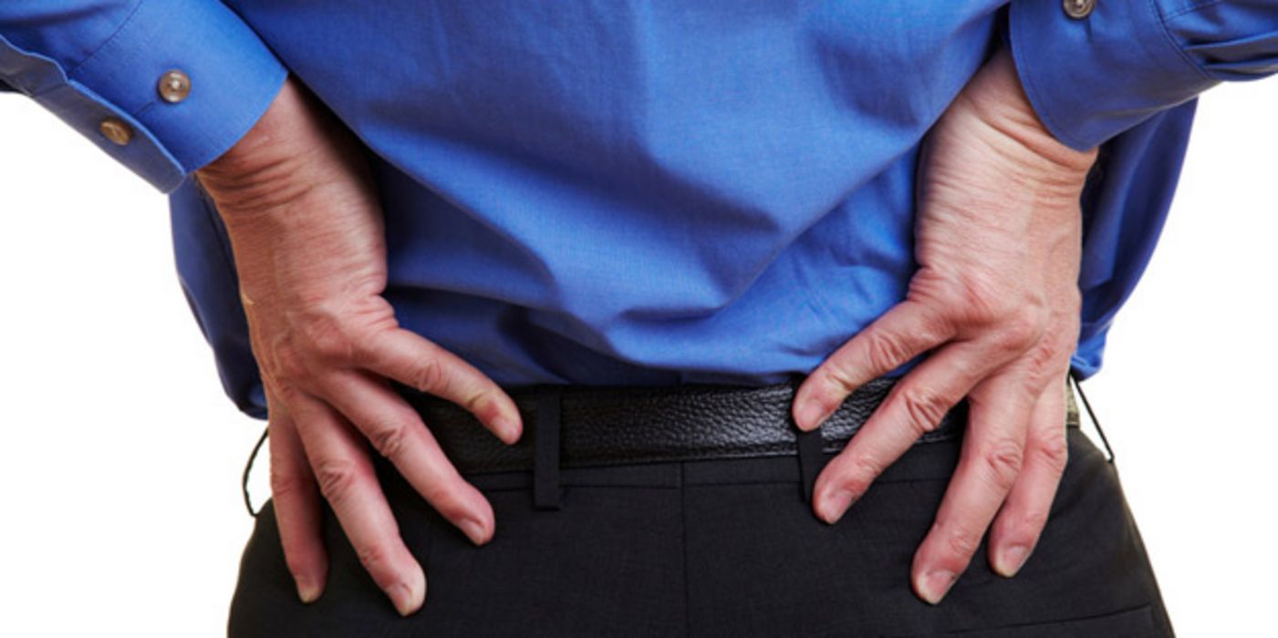 Rückenansicht eines Mannes in Anzughose und blauem Hemd, der sich den Rücken hält