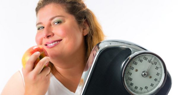 Übergewichtige Frau mit Waage und Apfel in der Hand