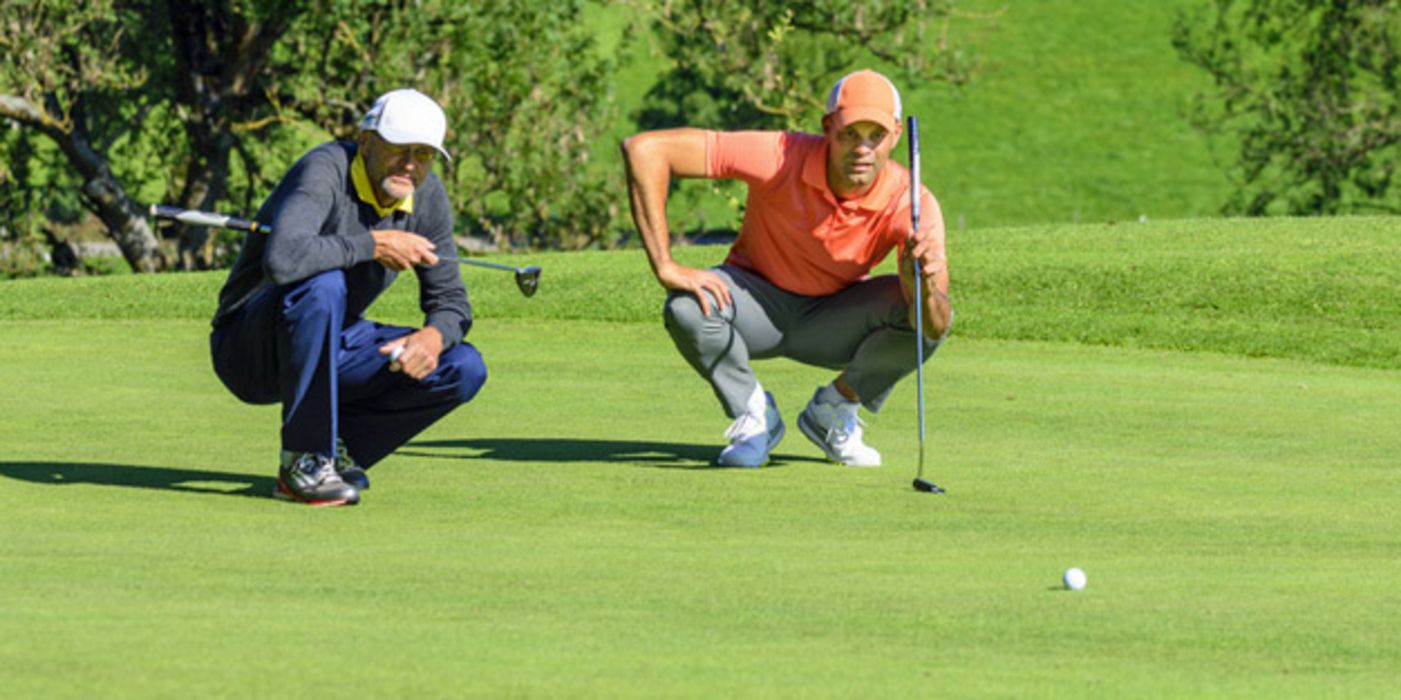 Zwei Golfer hocken auf dem Grün eines Golfplatzes und beurteilen die Situation
