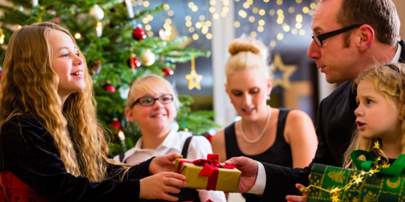 Festlich gekleidete Eltern und zwei Kinder (Mädchen) bei der Bescherung, Weihnachtsbaum im Hintergrund