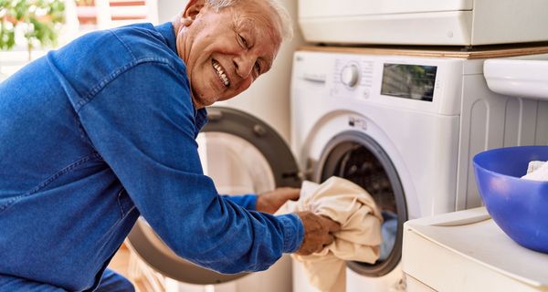 Senior, räumt eine Waschmaschine ein.