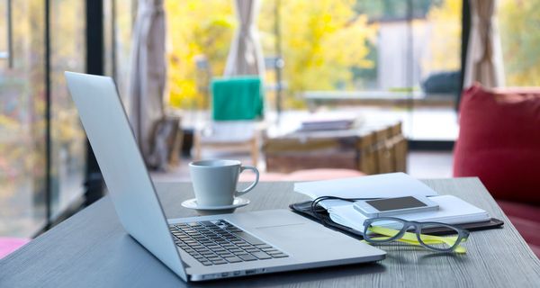 Schreibtisch mit Laptop, Kaffeetasse und Brille.