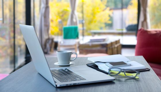 Schreibtisch mit Laptop, Kaffeetasse und Brille.