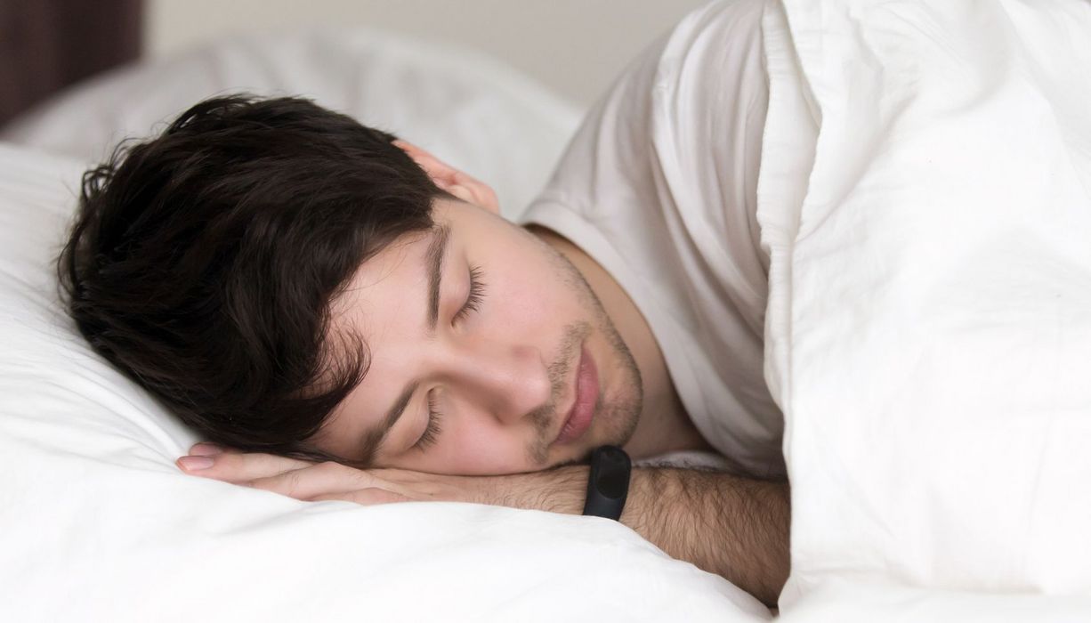 Junger Mann schläft mit Fitnesstracker am Handgelenk.