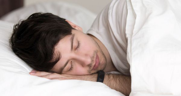 Junger Mann schläft mit Fitnesstracker am Handgelenk.