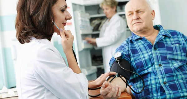Jüngere dunkelhaarige Ärztin misst älterem Patienten den Blutdruck
