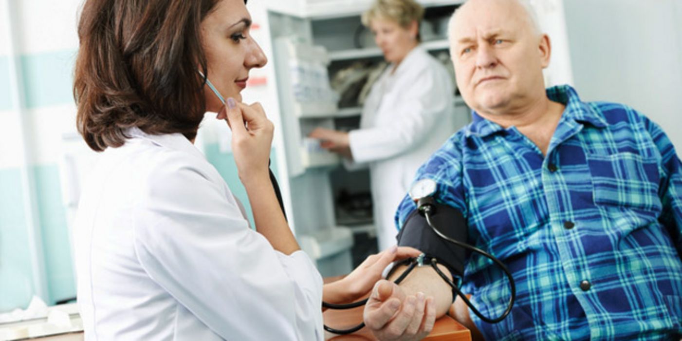 Jüngere dunkelhaarige Ärztin misst älterem Patienten den Blutdruck