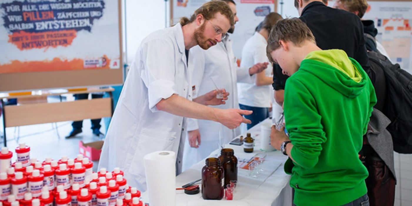 Schüler steht an einem Informationsstand und hält ein kleines Becherglas in der Hand