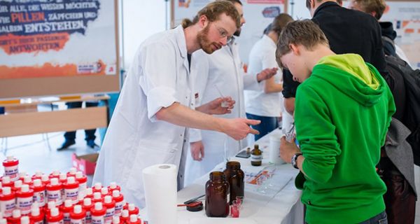 Schüler steht an einem Informationsstand und hält ein kleines Becherglas in der Hand