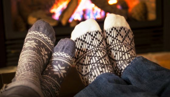 Zwei Fußpaare mit Wintersocken strecken sich einem prasselnden Kaminfeuer entgegen