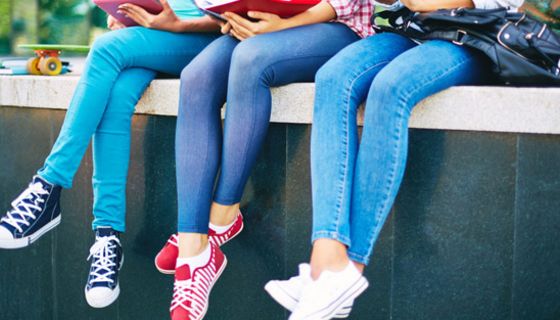 Drei junge, schlanke Frauen sitzen auf einer Mauer, tragen enge Jeans.
