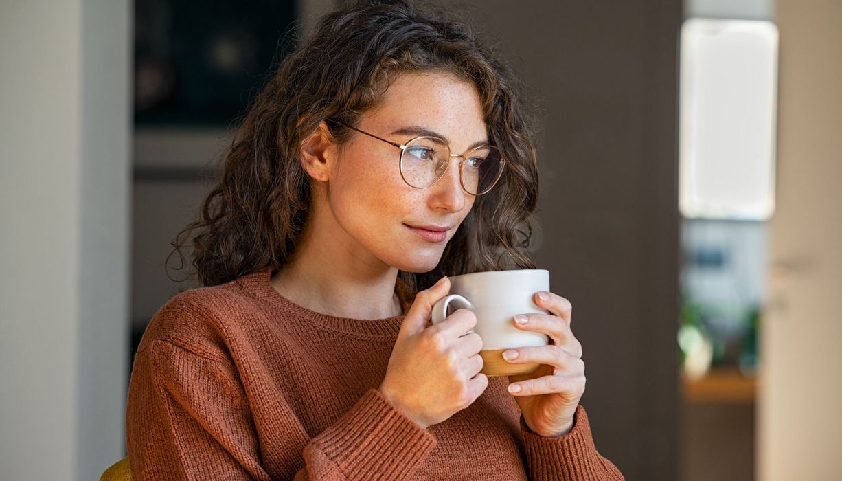Junge Frau mit Brille trinkt Tee.