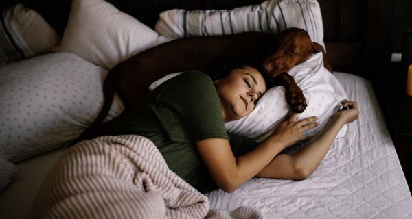 Frau, schläft mit einem Hund in einem Bett zusammen.
