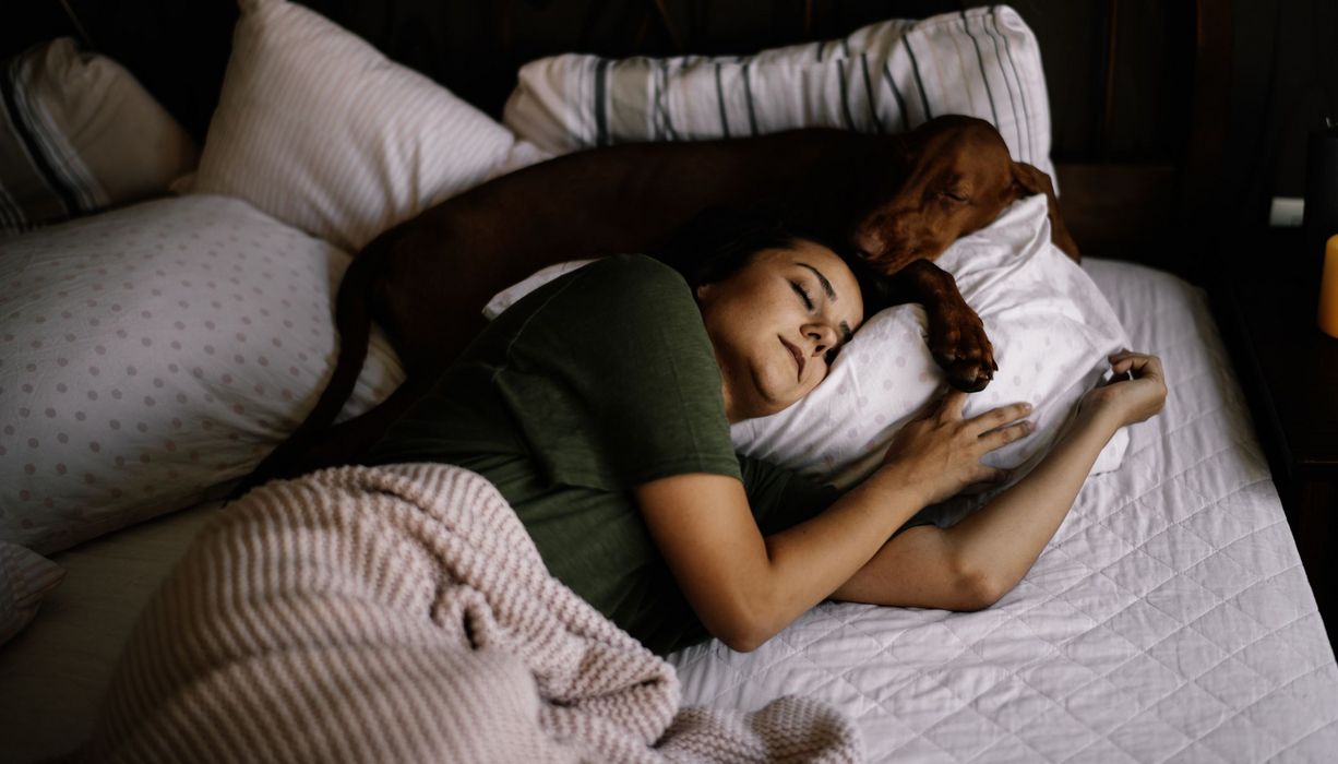 Frau, schläft mit einem Hund in einem Bett zusammen.