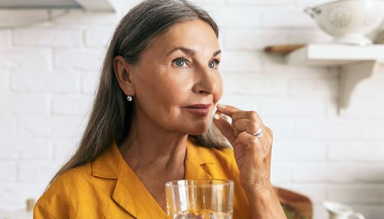 eine ältere Frau nimmt eine Kapsel und hält ein Glas Wasser in der Hand.