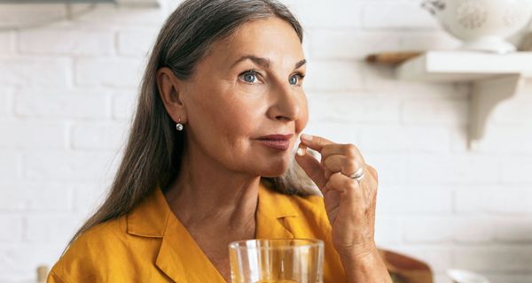 eine ältere Frau nimmt eine Kapsel und hält ein Glas Wasser in der Hand.