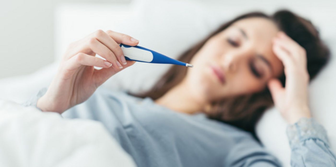 Frau, liegt im Bett mit Fieberthermometer.