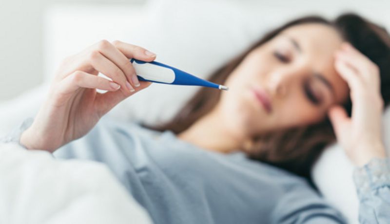Frau, liegt im Bett mit Fieberthermometer.