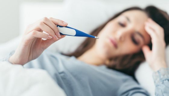 Frau, liegt im Bett mit Fieberthermometer.