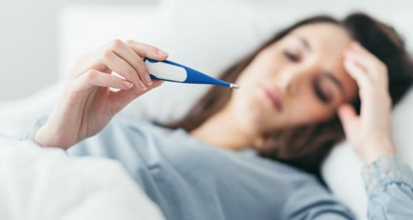 Frau, liegt im Bett mit Fieberthermometer.