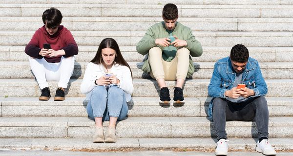Vier Jugendliche, sitzen auf einer Treppe und schauen auf das Smartphone.