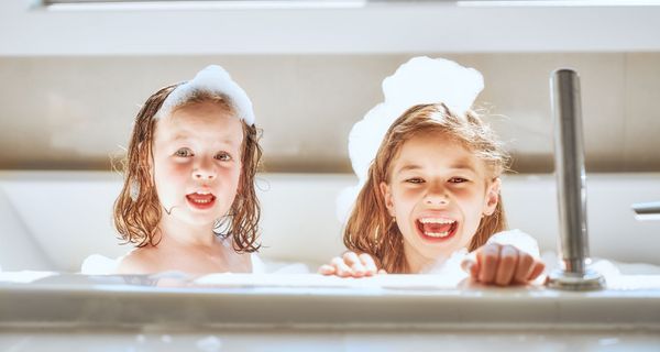 Zwei Mädchen mit Schaum im Gesicht in der Badewanne.