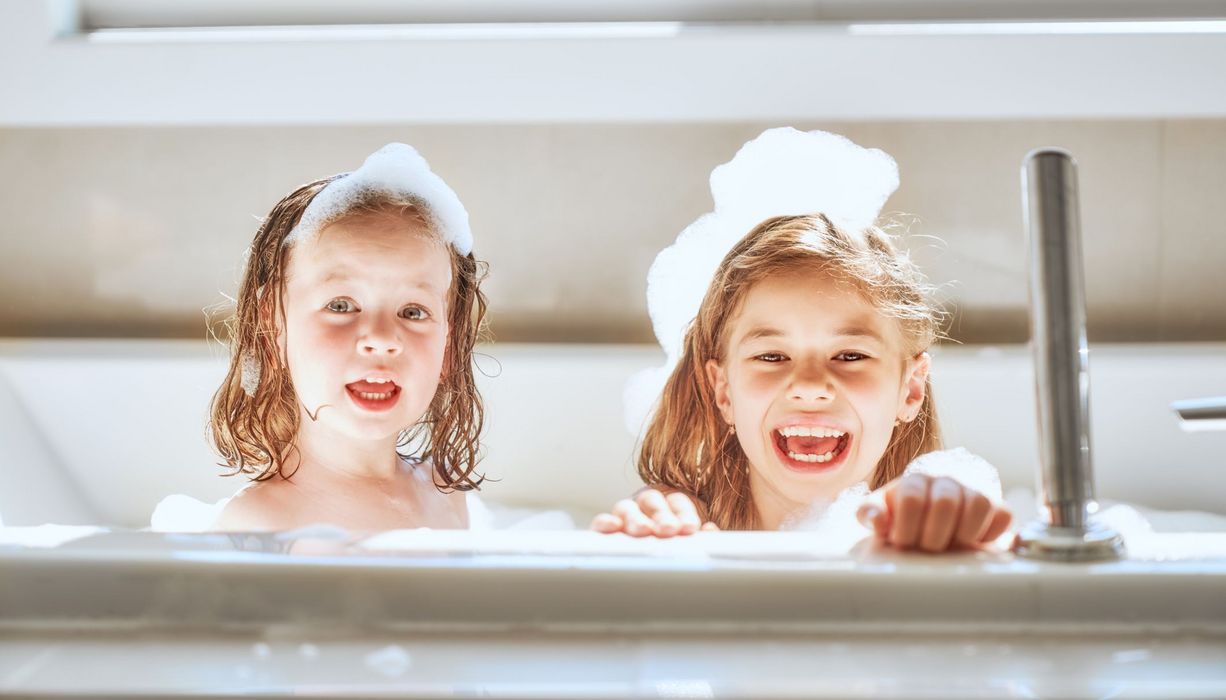 Zwei Mädchen mit Schaum im Gesicht in der Badewanne.
