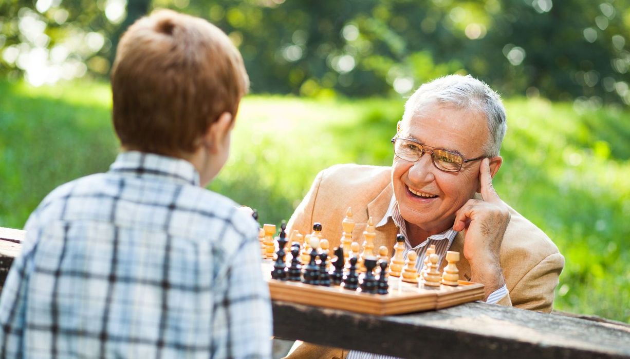 Opa speilt mit seinem Enkelsohn Schach und sieht dabei sehr aufmerksam und glücklich aus. 