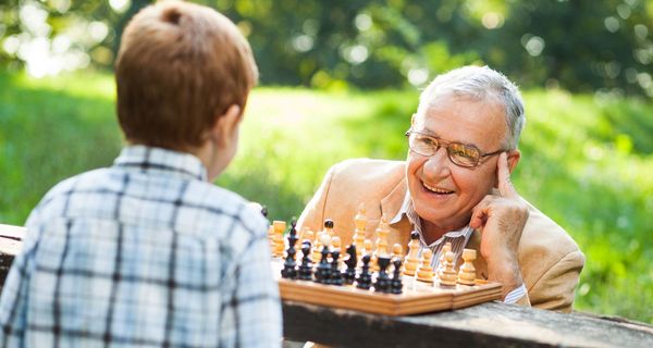 Opa speilt mit seinem Enkelsohn Schach und sieht dabei sehr aufmerksam und glücklich aus. 
