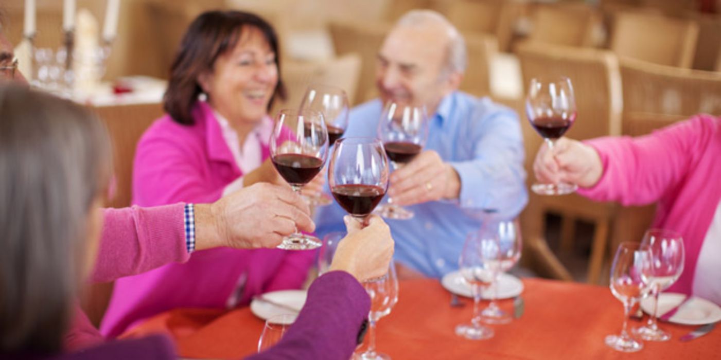 Runde mittelalter Menschen sitzt am Tisch und prostet sich mit Rotweingläsern zu