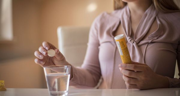 Frau, ist im Begriff, eine Brausetablette in ein Glas Wasser zu geben.