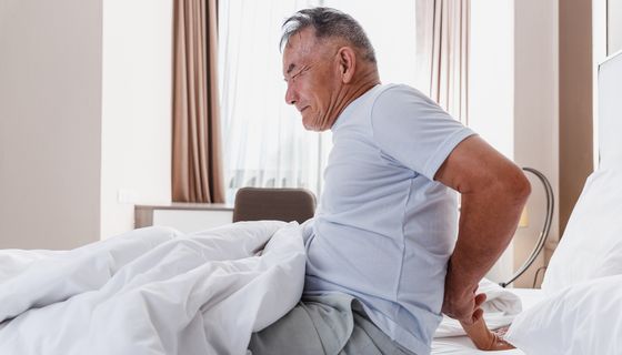 Mann, steht mit Rückenschmerzen aus dem Bett auf.